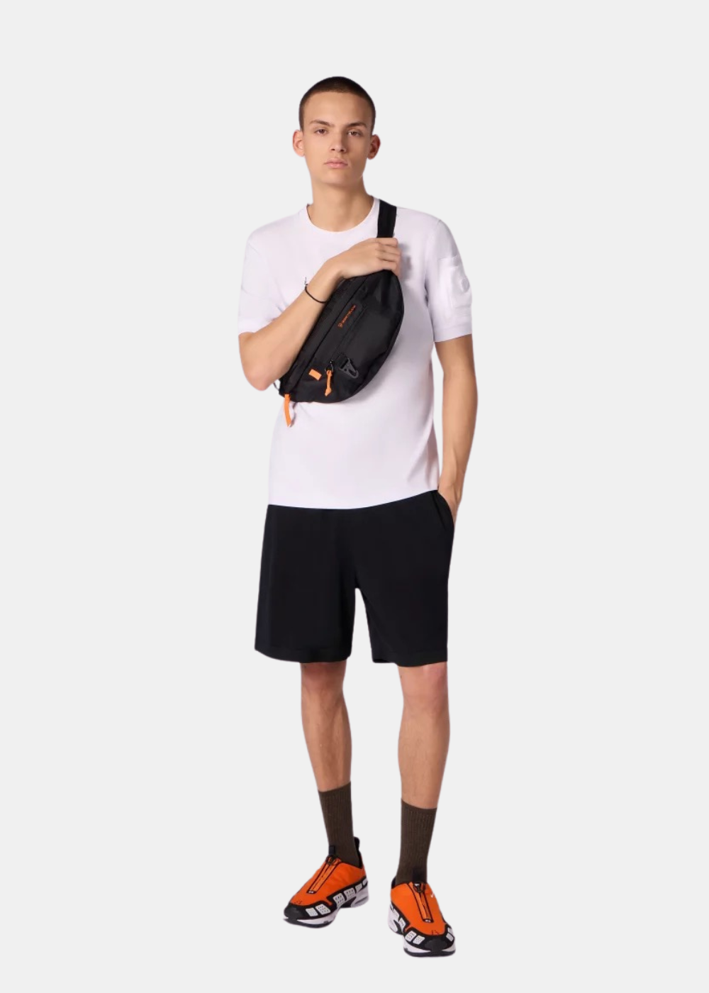 Un homme porte le short en maille noir Gertrude Isidore avec un t-shirt blanc et un sac banane noir.