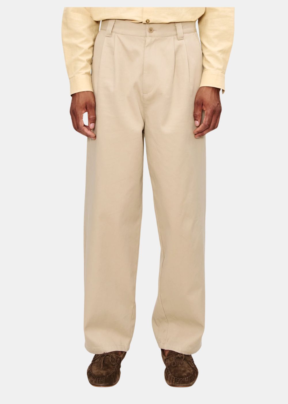 Pantalon beige A.P.C. à pinces et coupe droite porté de face avec une chemise jaune pâle.