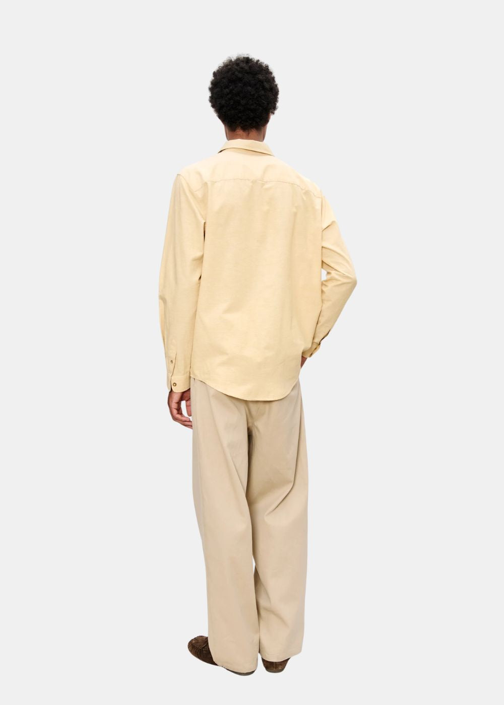 Silhouette complète de dos montrant le tombé droit du pantalon beige A.P.C. et l'ensemble du look.
