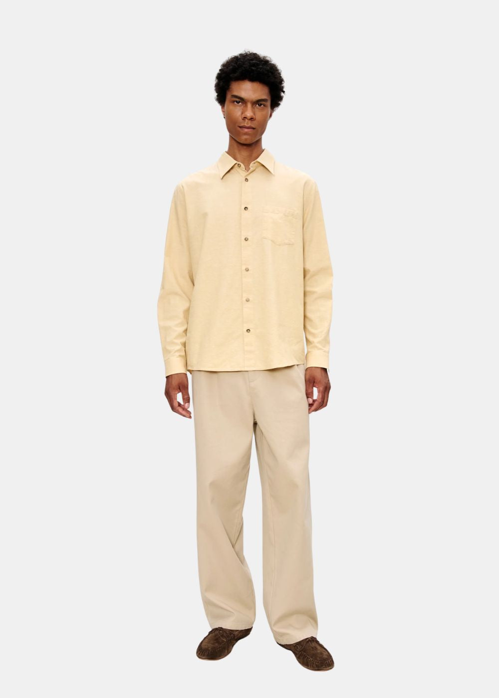 Look complet de face présentant le pantalon beige A.P.C. avec une chemise jaune et des mocassins marron.