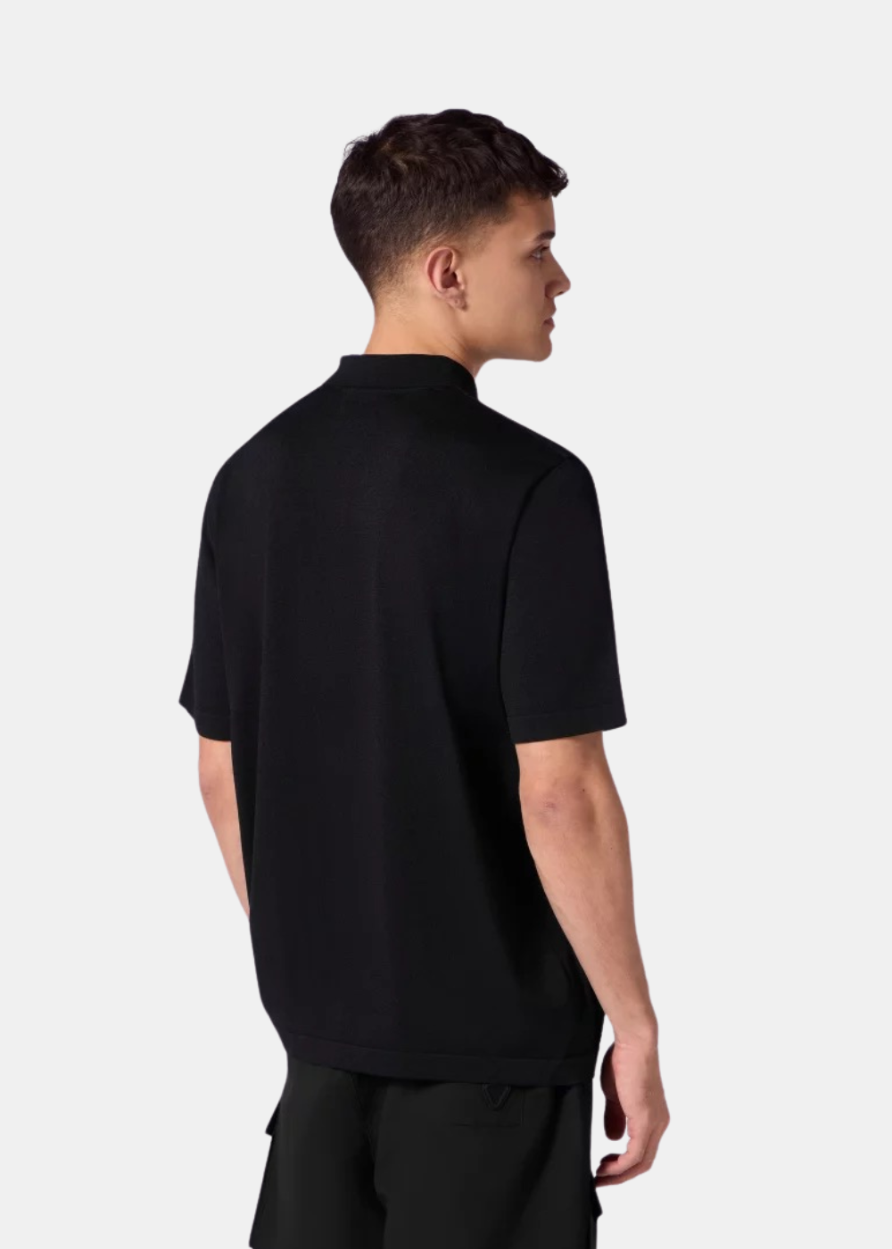 Vue de dos d'un homme portant le polo oversize en maille noir Gertrude Jude avec un short assorti en maille noir.