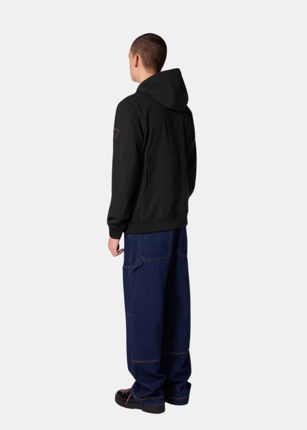 Vue de dos d'un homme portant la veste technique Ronaldo noire Gertrude avec capuche levée et un jean large.