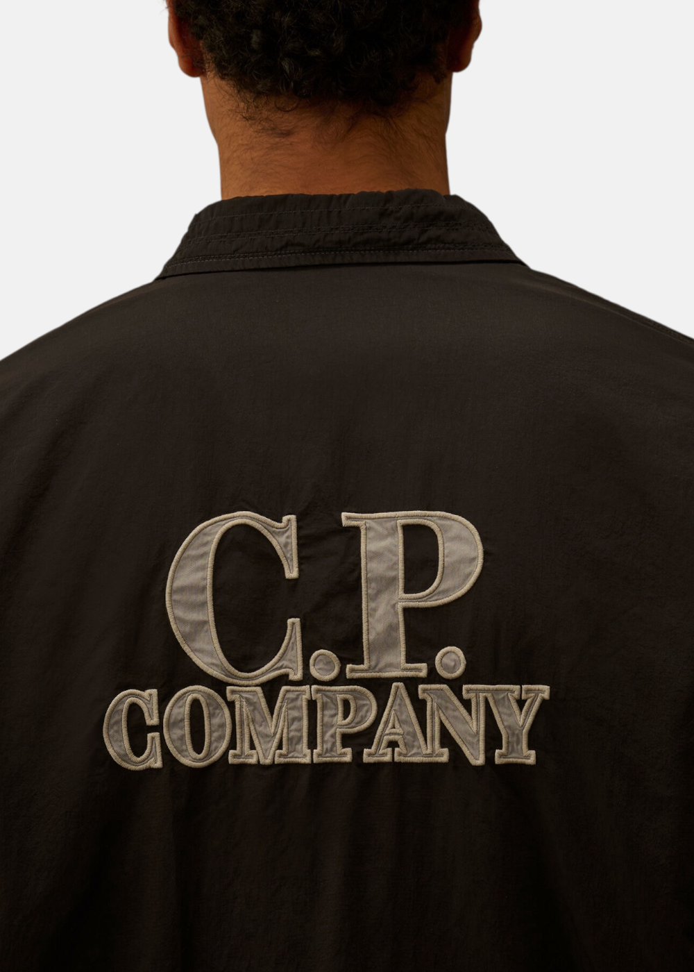 Zoom sur le grand logo brodé C.P. Company texturé gris clair au dos de la surchemise noire.