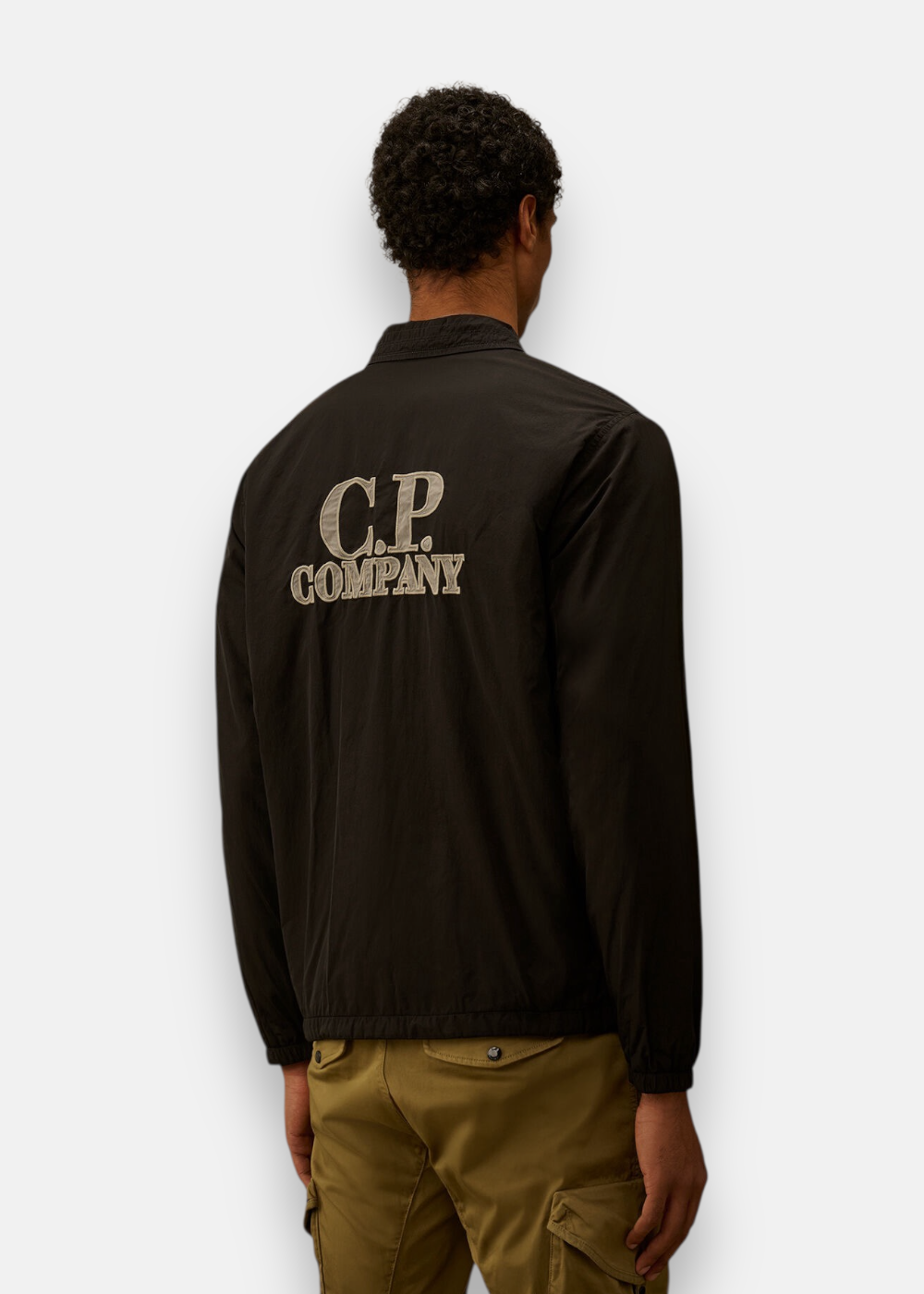 Vue de dos d'un homme portant la surchemise noire avec le grand logo C.P. Company brodé au centre.
