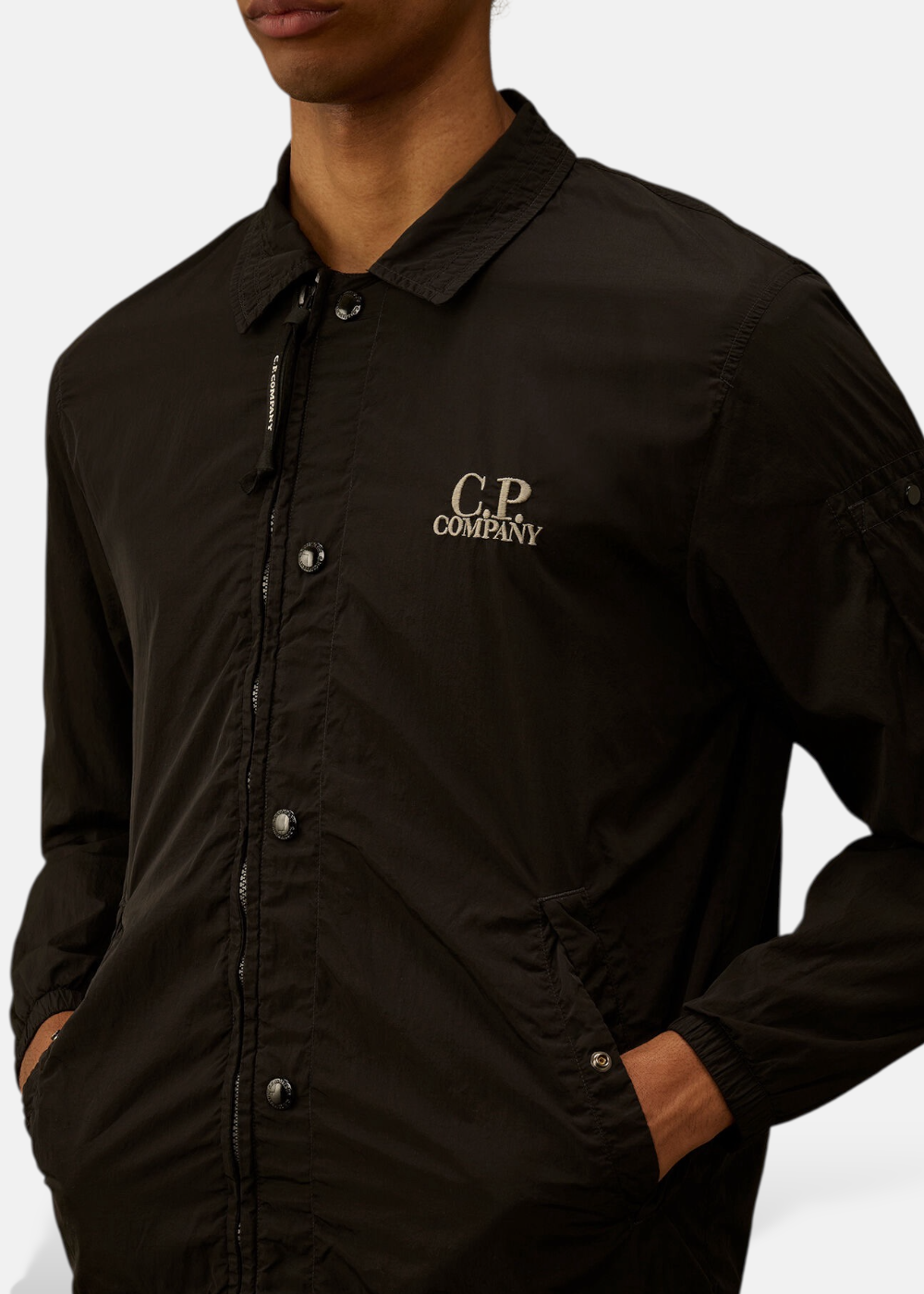 Détail du col et de la poitrine de la surchemise noire montrant le logo C.P. Company brodé en gris.