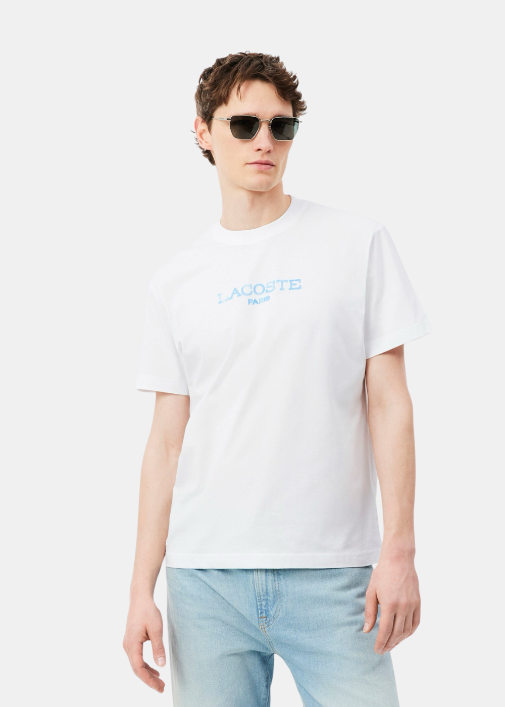 T-shirt Lacoste blanc porté par un homme avec un jean bleu clair et des lunettes de soleil. Vue de face sur fond neutre.