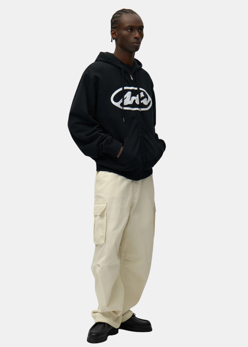 Look complet avec hoodie zippé noir Arte Antwerp, pantalon cargo beige et chaussures noires, vue de trois-quarts.