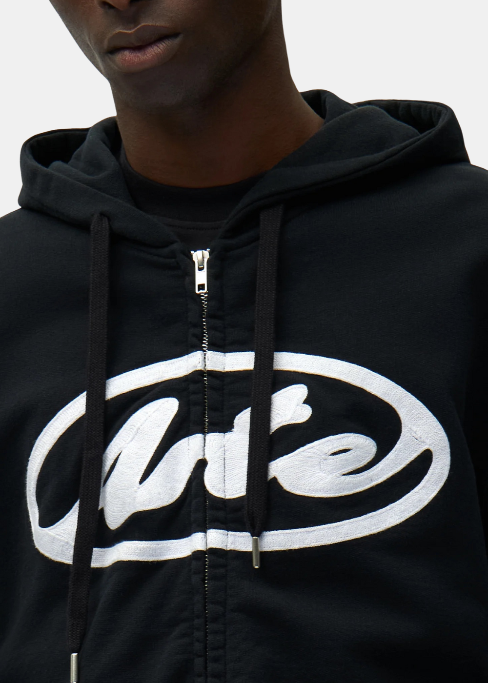 Zoom sur le logo circulaire blanc brodé et la fermeture éclair métallique d'un hoodie zippé noir Arte Antwerp.