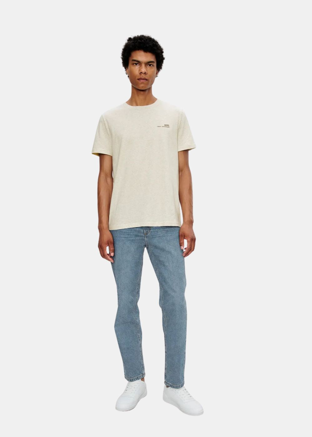 Mannequin homme portant le jean bleu délavé A.P.C. avec un t-shirt beige et des baskets blanches.