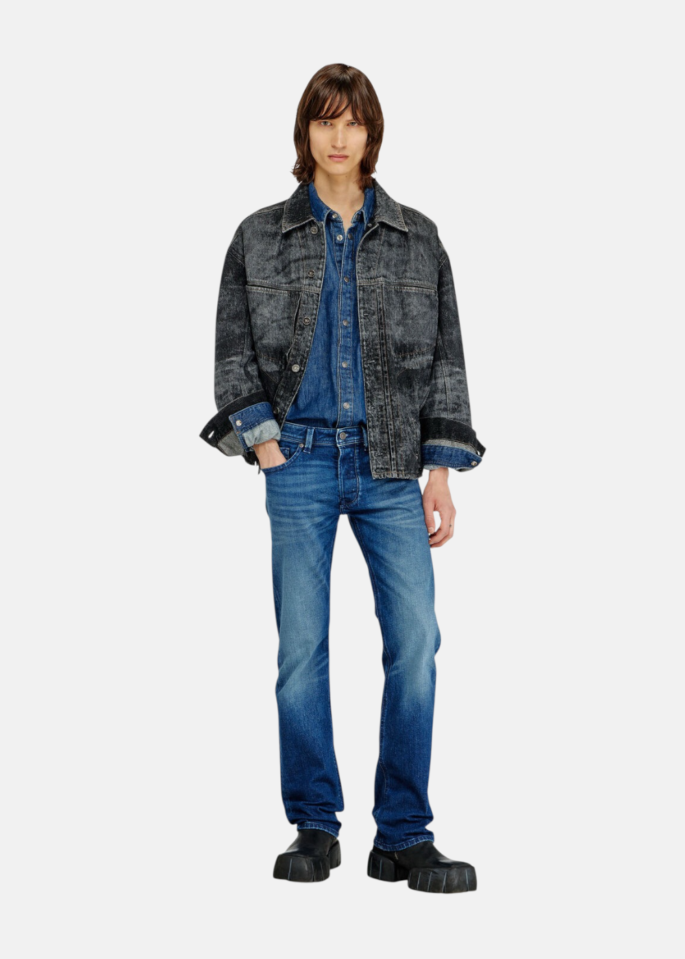 Silhouette complète montrant un mannequin avec le jean bleu Diesel 1985 Larkee, une chemise en denim, une veste en jean délavée noire et des bottines
