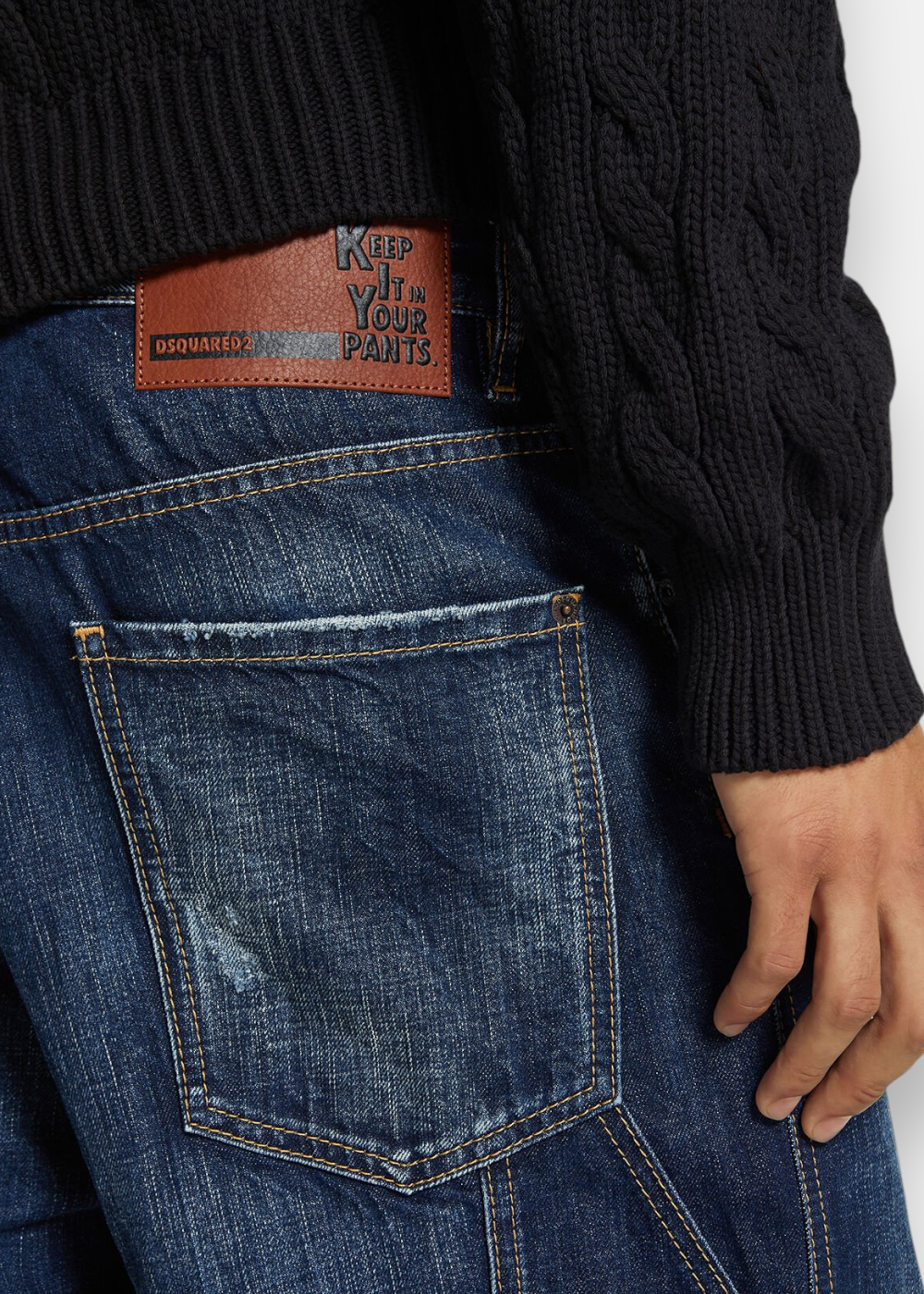 Gros plan sur l'arrière du jean Dsquared2 montrant le patch en cuir marron Keep It In Your Pants et la maille du pull noir.