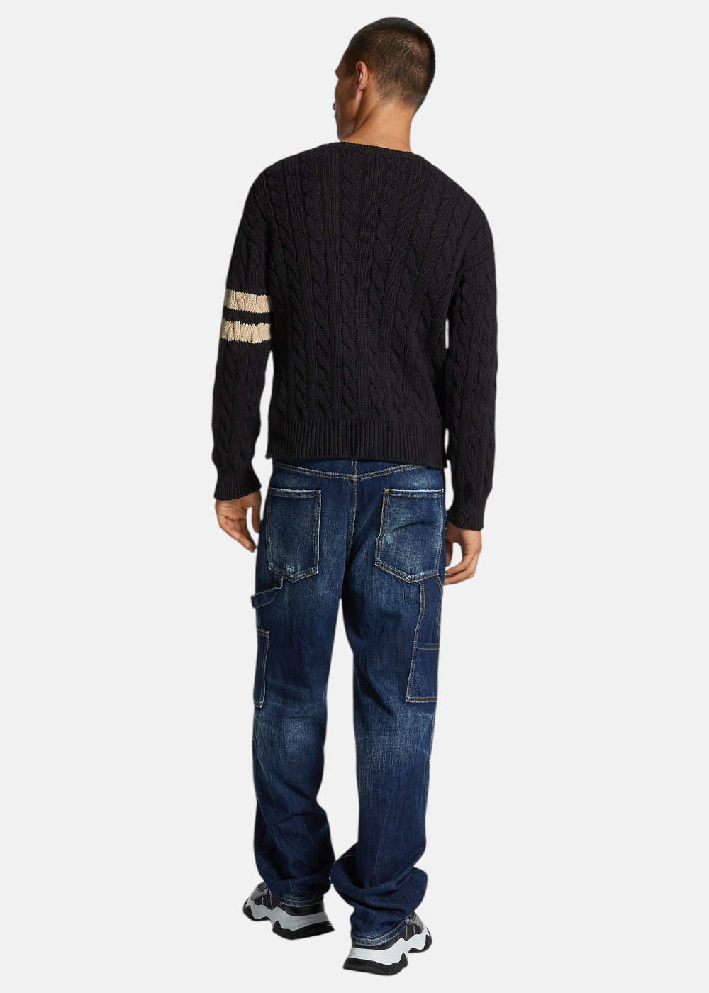 Mannequin de dos portant le jean carpenter Dsquared2 bleu avec un pull en maille torsadée noir et des baskets.