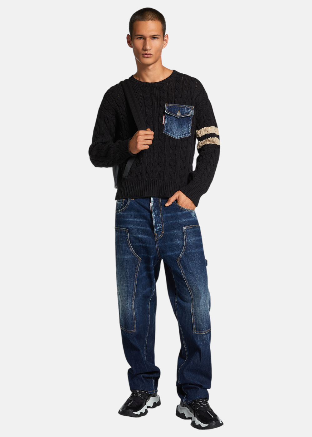 Mannequin de face portant le jean carpenter Dsquared2 bleu, un pull noir avec poche denim et des baskets volumineuses.