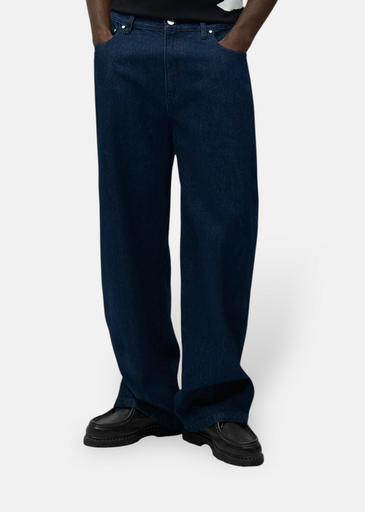 Focus sur le bas d'un jean denim brut foncé porté avec des chaussures noires, vue de face.