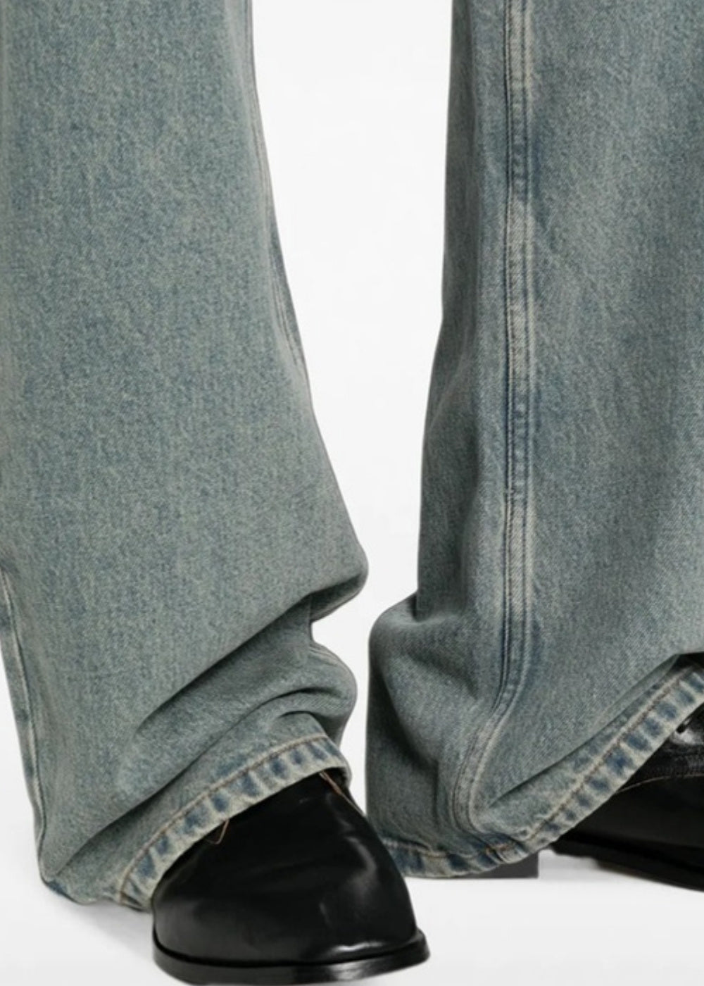 Gros plan sur le bas de jambe d'un jean A.P.C. IAL bleu délavé tombant sur des chaussures en cuir noir.
