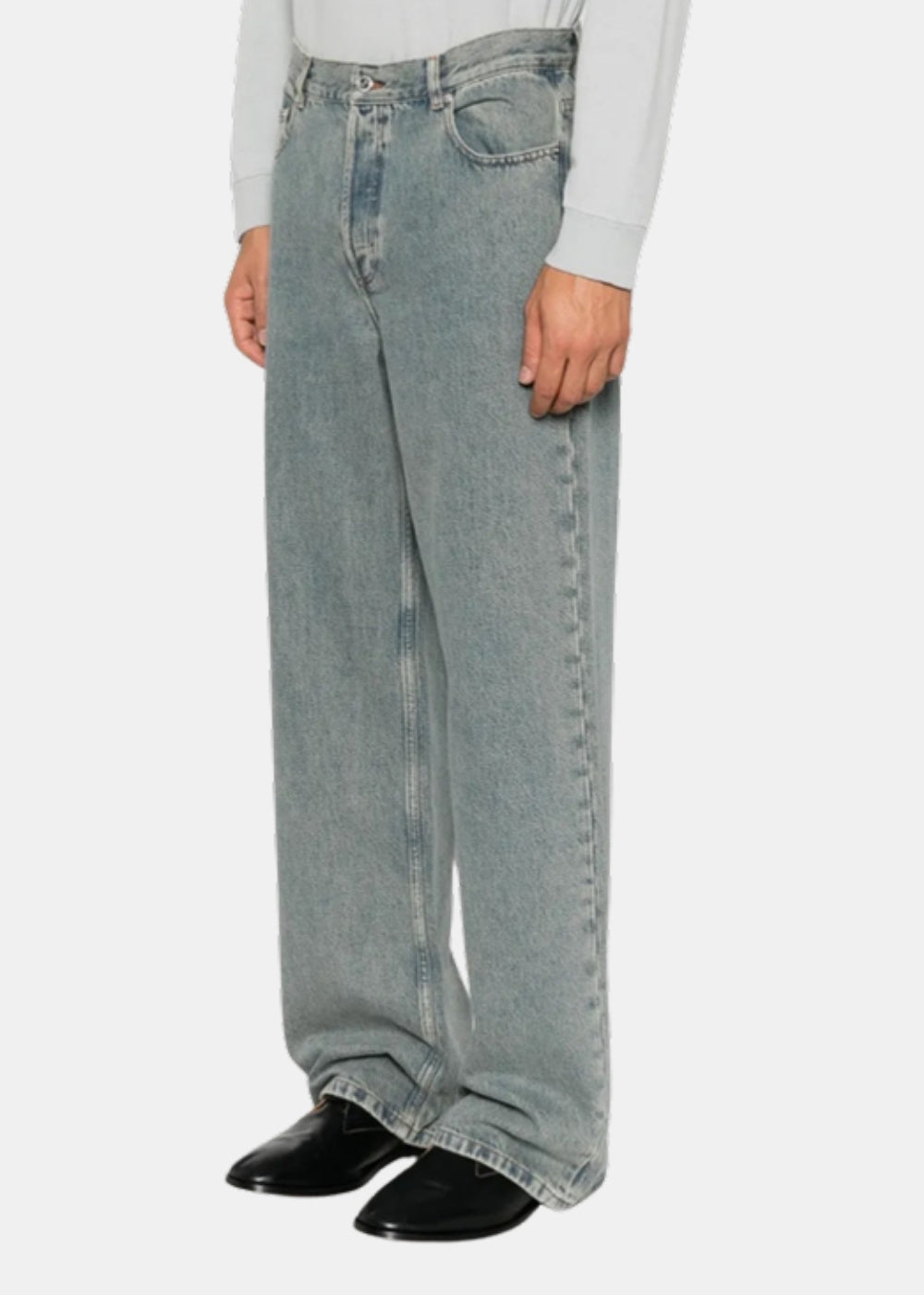 Porté de profil d'un jean A.P.C. IAL bleu délavé à jambe droite, vu à la taille avec chaussures noires.
