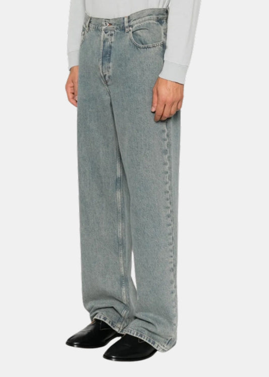 Porté de profil d'un jean A.P.C. IAL bleu délavé à jambe droite, vu à la taille avec chaussures noires.