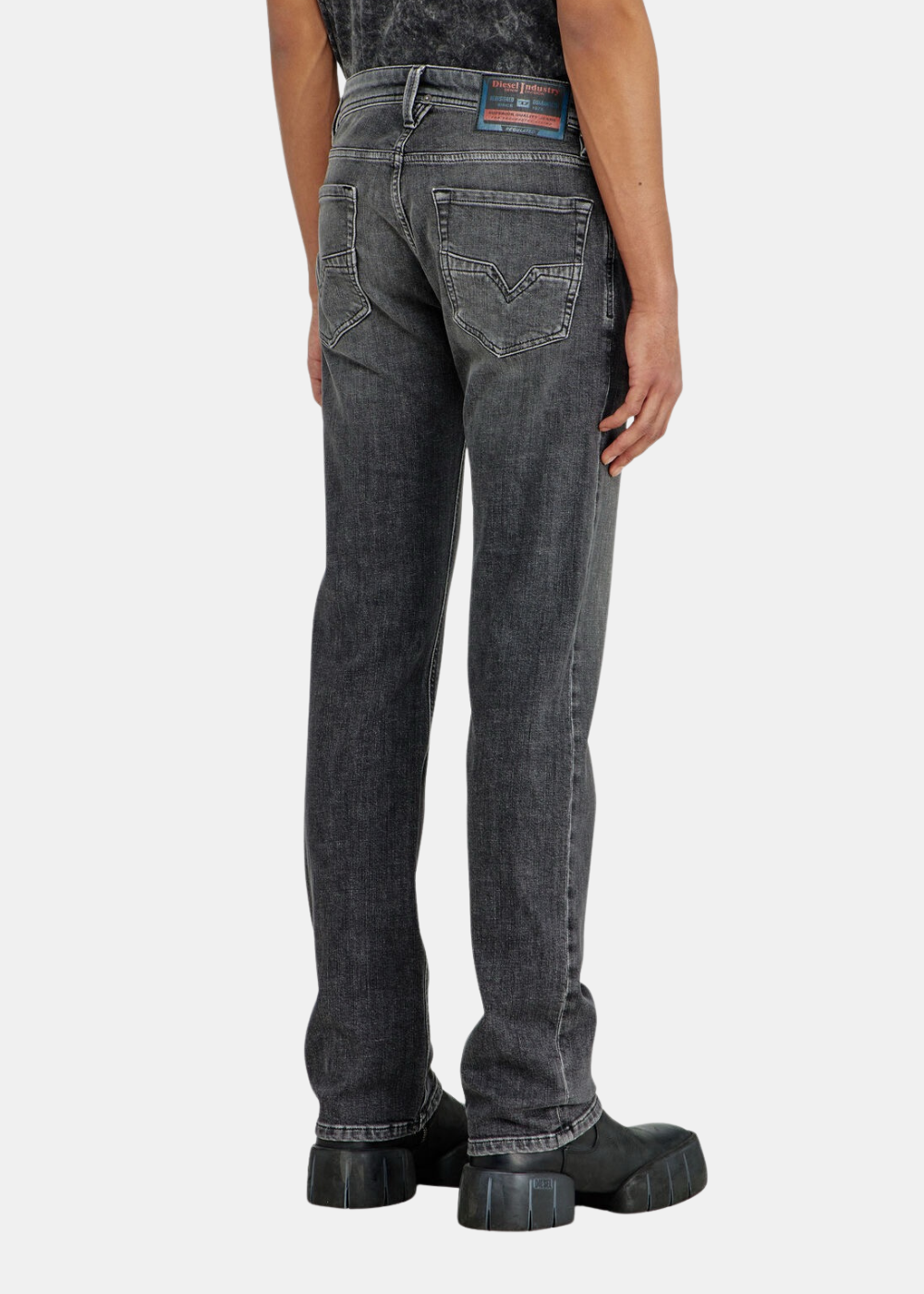 Gros plan sur le bas du corps d'un mannequin portant le jean Diesel gris délavé, de dos.