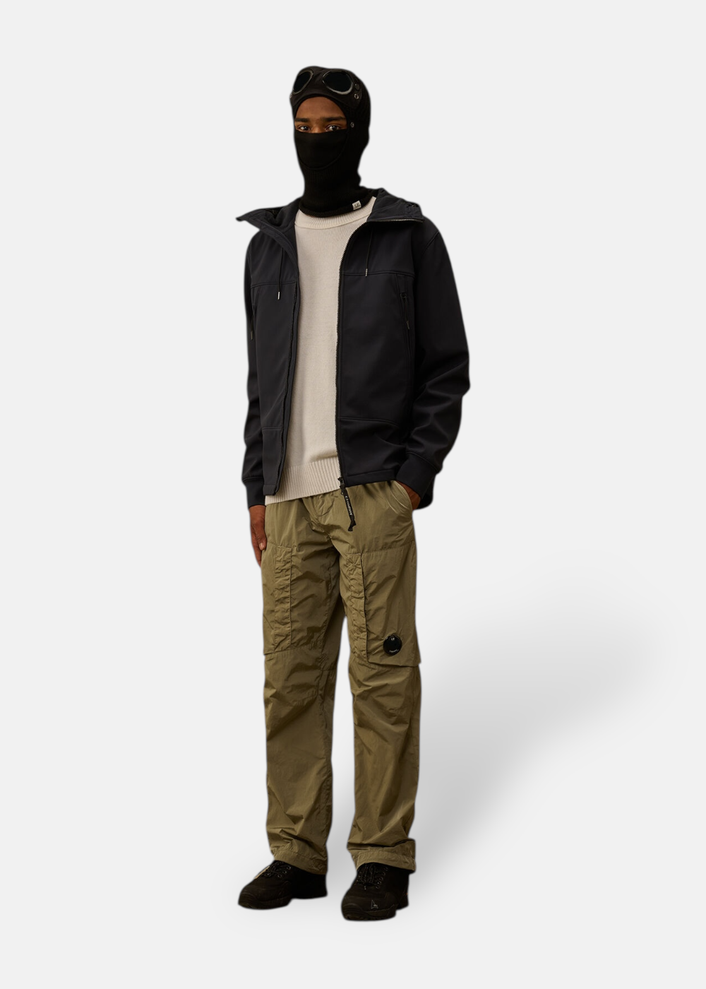 Look complet C.P. Company : Homme portant le pull Lambswool sous un blouson bleu marine avec cagoule et pantalon cargo.