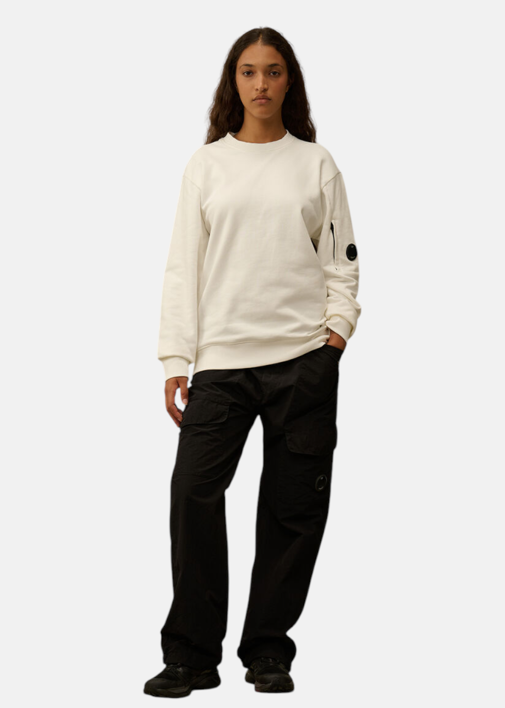 Look complet femme : sweat C.P. Company blanc cassé avec un pantalon cargo noir.