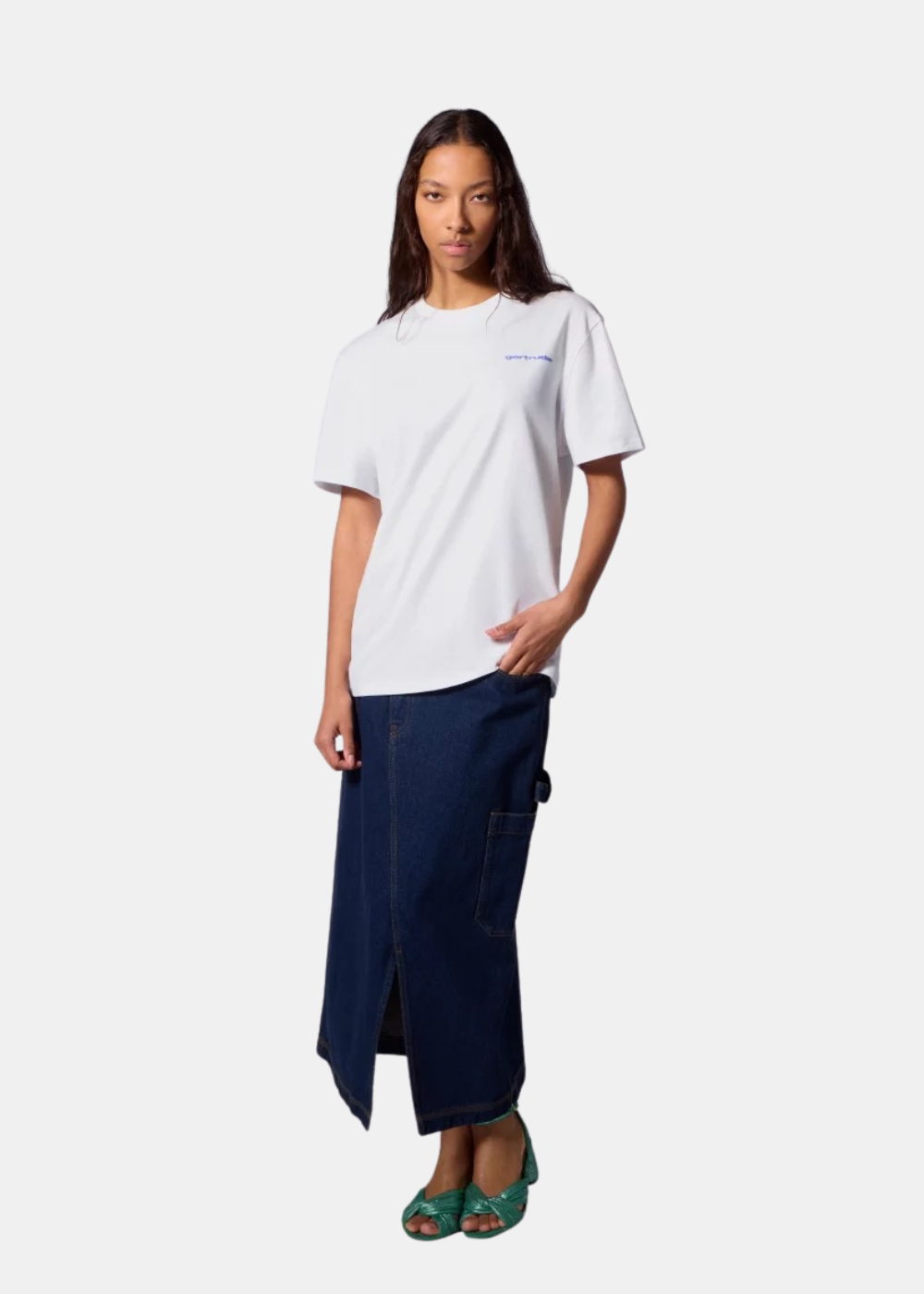 Mannequin femme de face portant le t-shirt blanc Gertrude, une longue jupe en jean bleu foncé fendue et des sandales vertes.