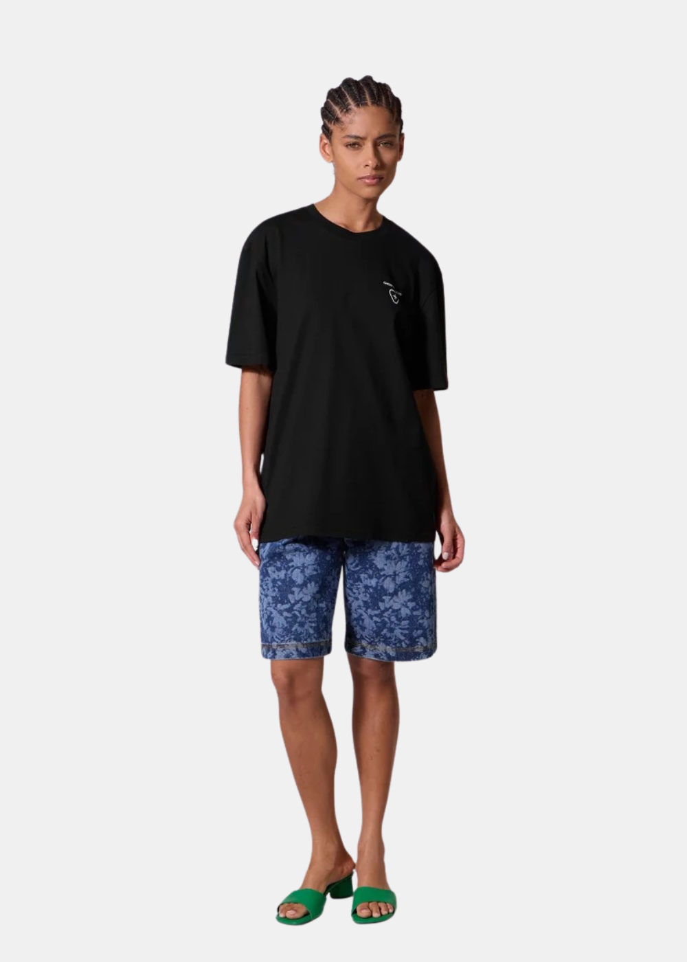 Mannequin femme de face portant le t-shirt noir Gertrude, un short imprimé bleu et des sandales vertes, montrant le logo de poitrine.