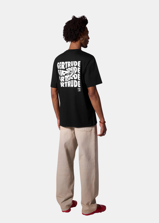 Mannequin homme de dos portant le t-shirt noir Gertrude imprimé, un jean large beige et des chaussures rouges, sur fond uni.