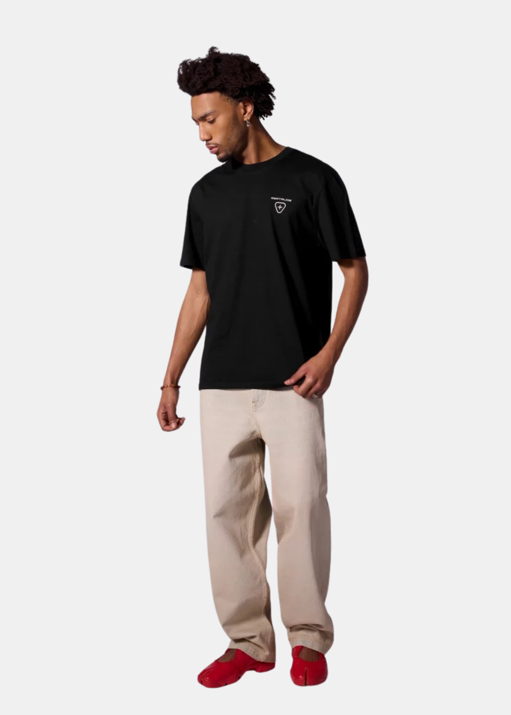 Mannequin homme de face portant le t-shirt noir Gertrude, un jean large beige et des chaussures rouges, montrant le logo de poitrine.