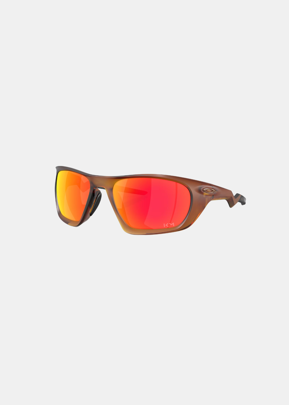 Packshot de trois-quarts face sur fond gris des lunettes Oakley Lateralis Kylian Mbappé, présentant sa monture marron translucide effet écaille, son logo ellipse doré et ses verres miroirs Prizm Ruby gravés du monogramme KM