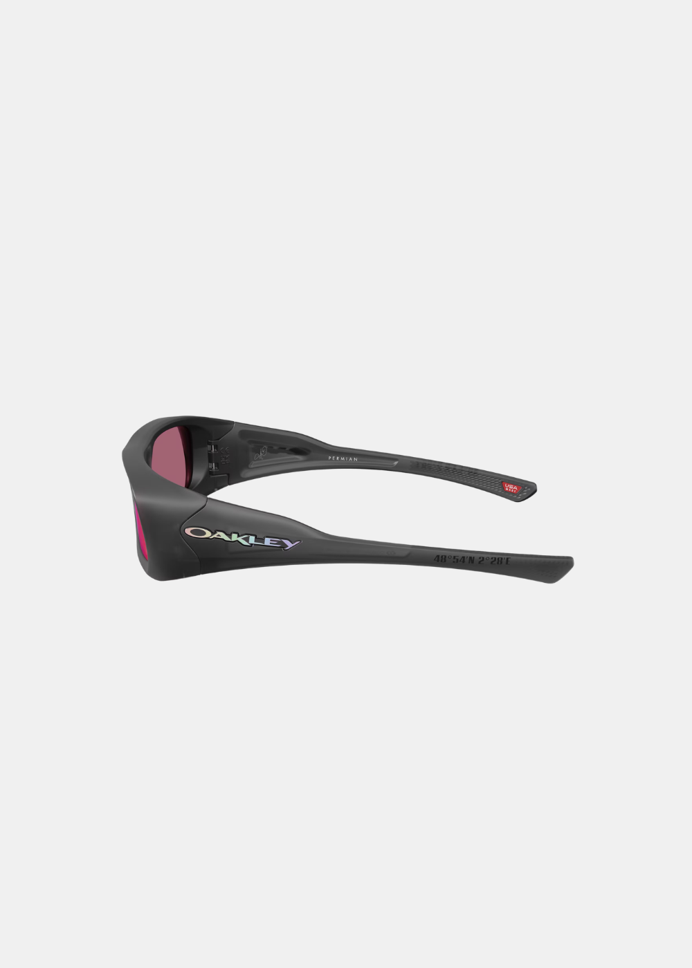 Packshot de profil des lunettes Oakley Permian Mbappé noires, affichant la large branche profilée ornée de l'inscription Oakley en relief irisé et des coordonnées géographiques gravées en noir à l'extrémité
