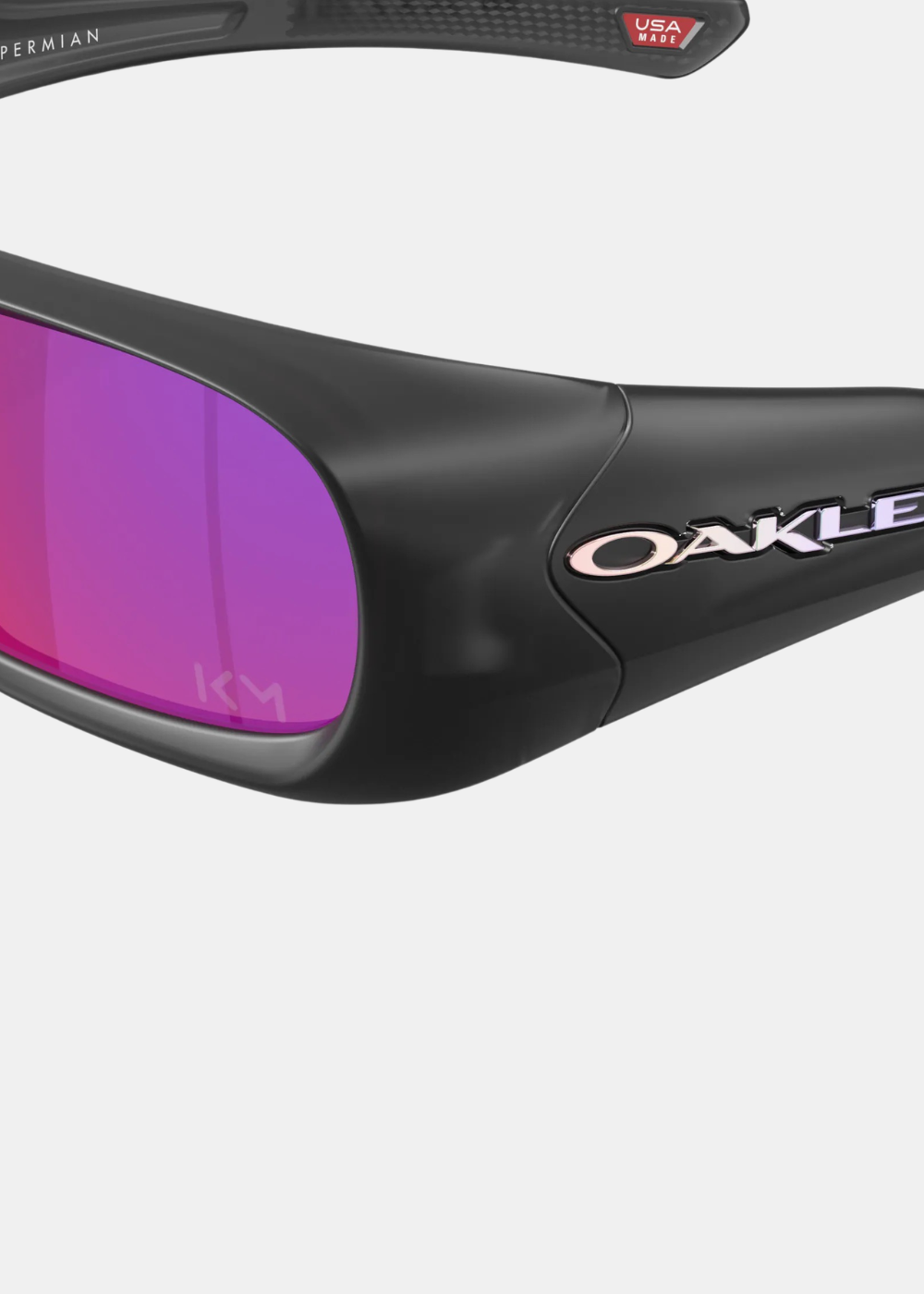 Gros plan détaillé sur le coin gauche des lunettes Oakley Permian Mbappé, mettant en valeur le lettrage Oakley chromé et holographique sur la branche noire, ainsi que le monogramme gravé KM au bas du verre miroir violet