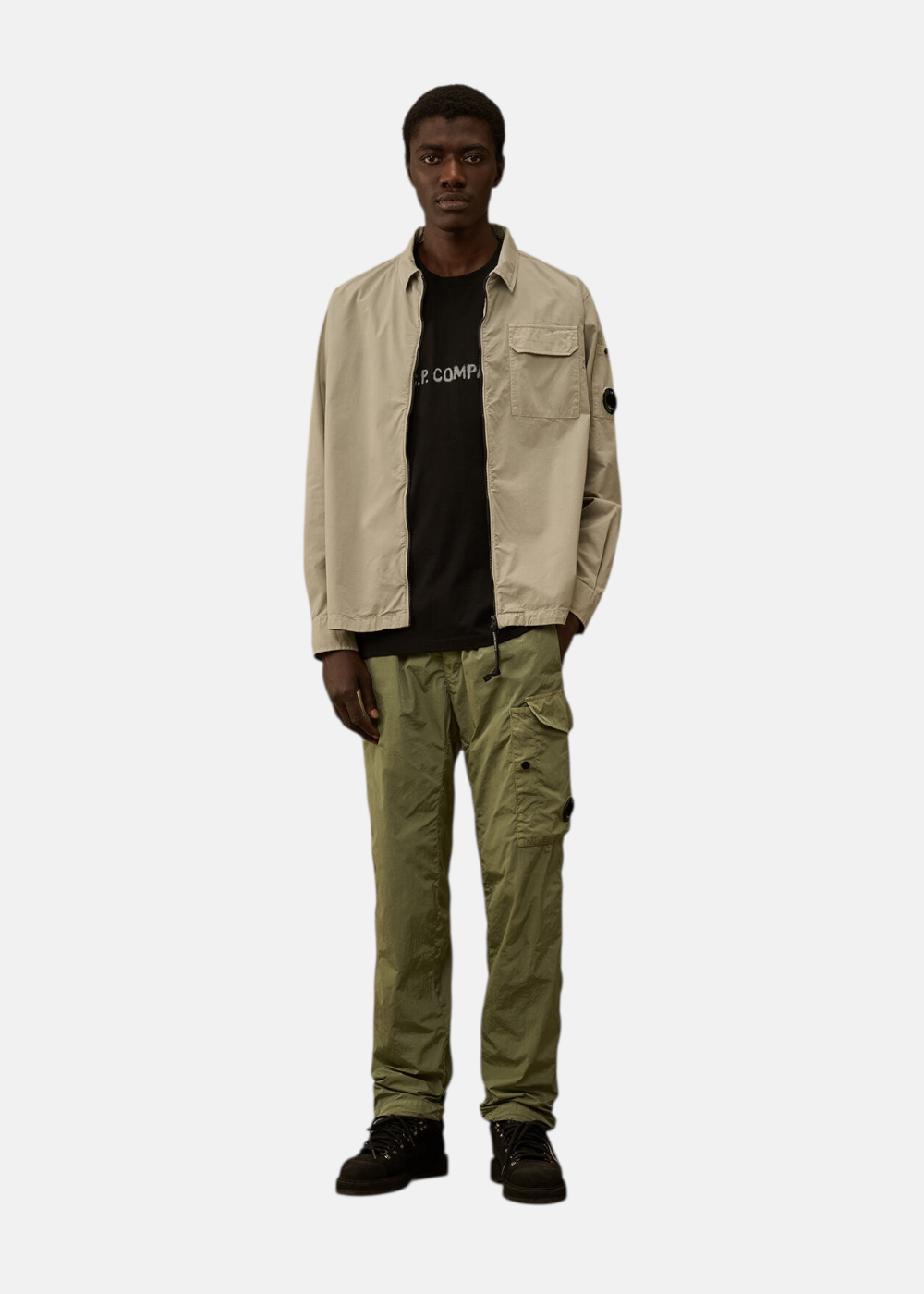 Look complet homme : surchemise C.P. Company zippée  beige sur un T-shirt noir avec un pantalon cargo vert.