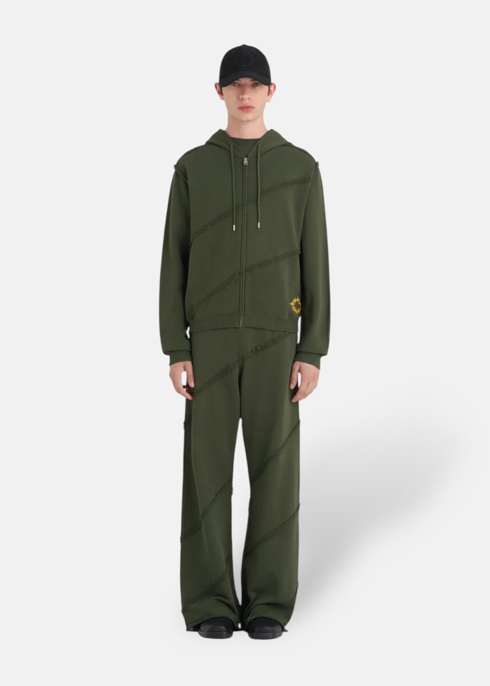 photo d'un mannequin portant le Sweat à capuche Zippé Études Studio vert forêt avec son pantalon assortie. cette photo mets en avant la coupe droite de ce sweat études