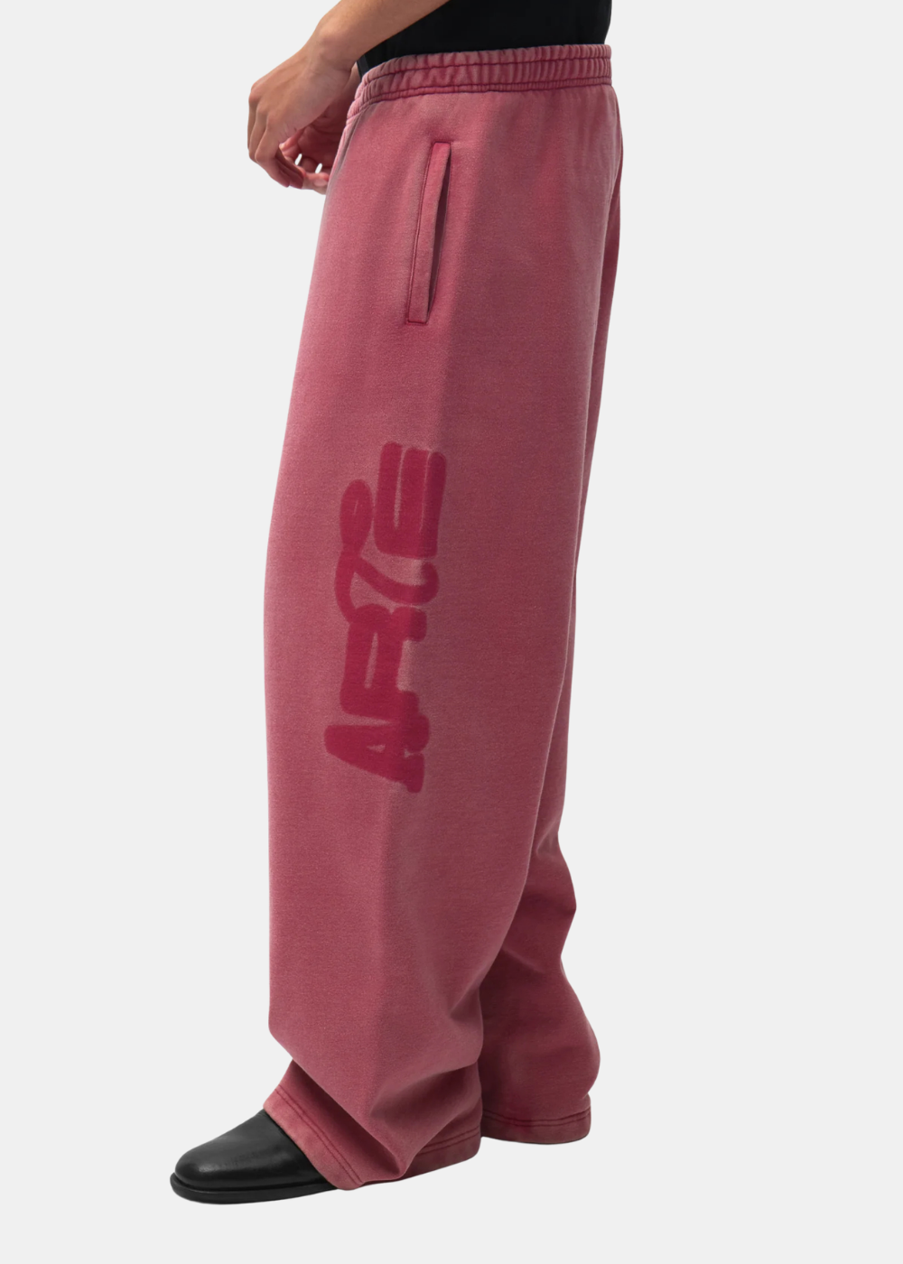 Gros plan sur le bas du pantalon de jogging ample rouge délavé Arte Antwerp porté avec des chaussures noires.