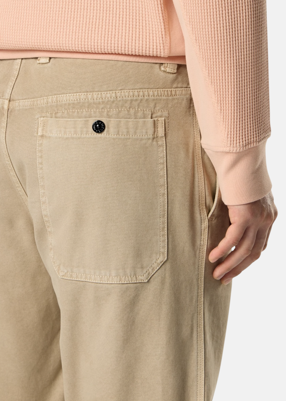 Zoom sur la poche arrière boutonnée d'un pantalon beige Stone Island effet old, porté avec un pull corail.