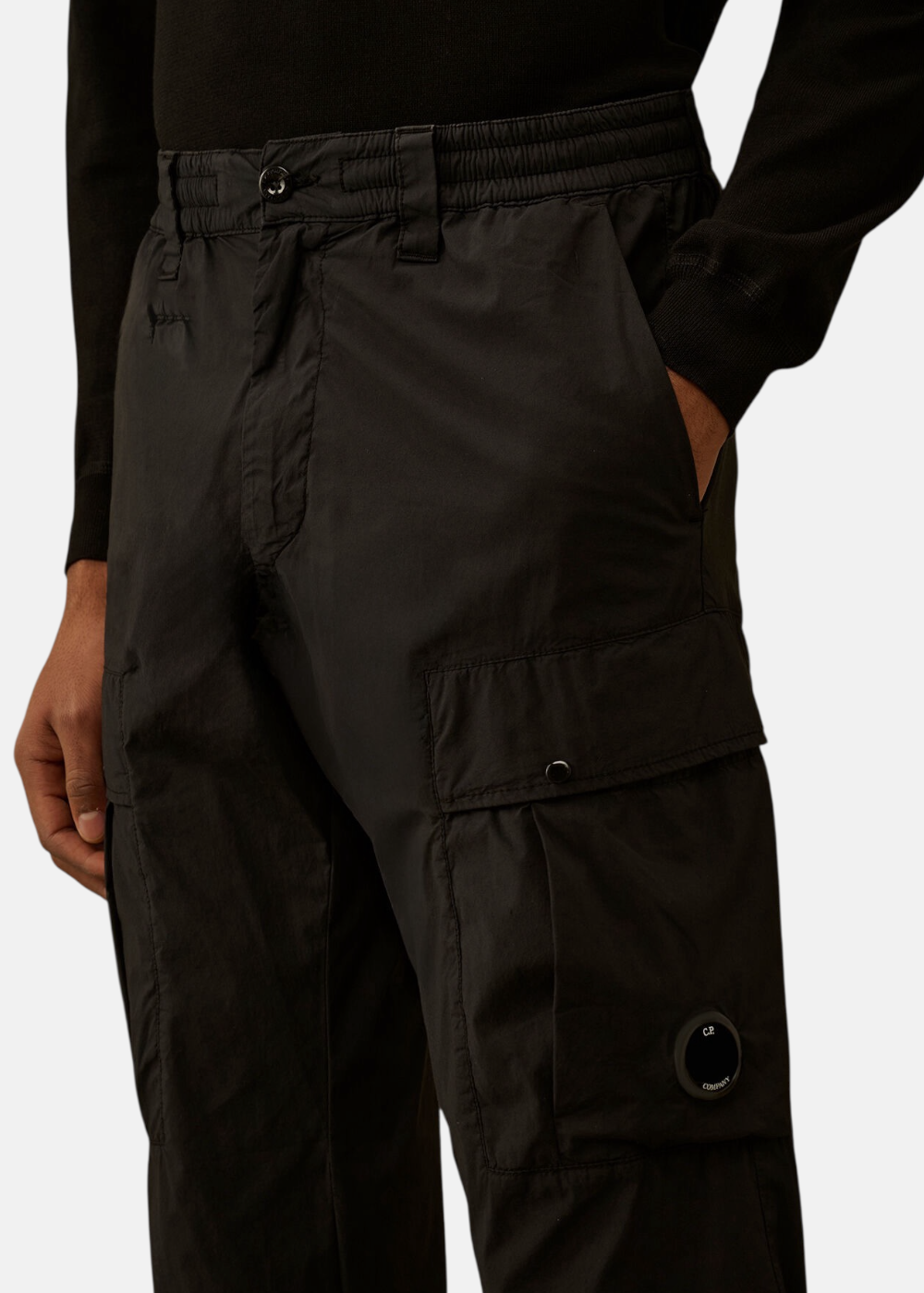 Zoom sur la poche cargo latérale du pantalon noir avec le verre de lunette Lens noir distinctif de C.P. Company.