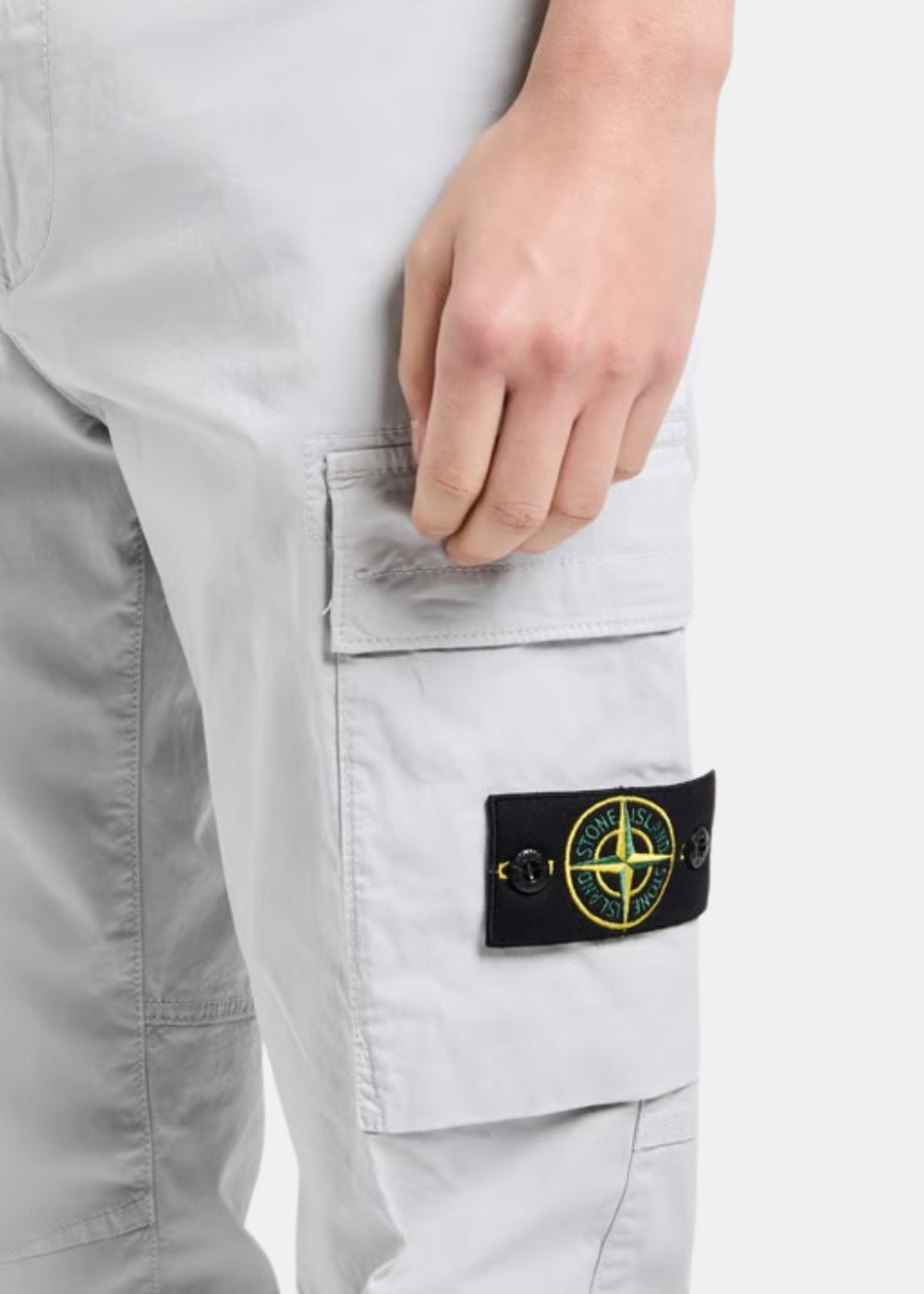 Gros plan de profil sur la poche latérale d'un pantalon cargo gris Stone Island porté, avec le badge boussole emblématique.