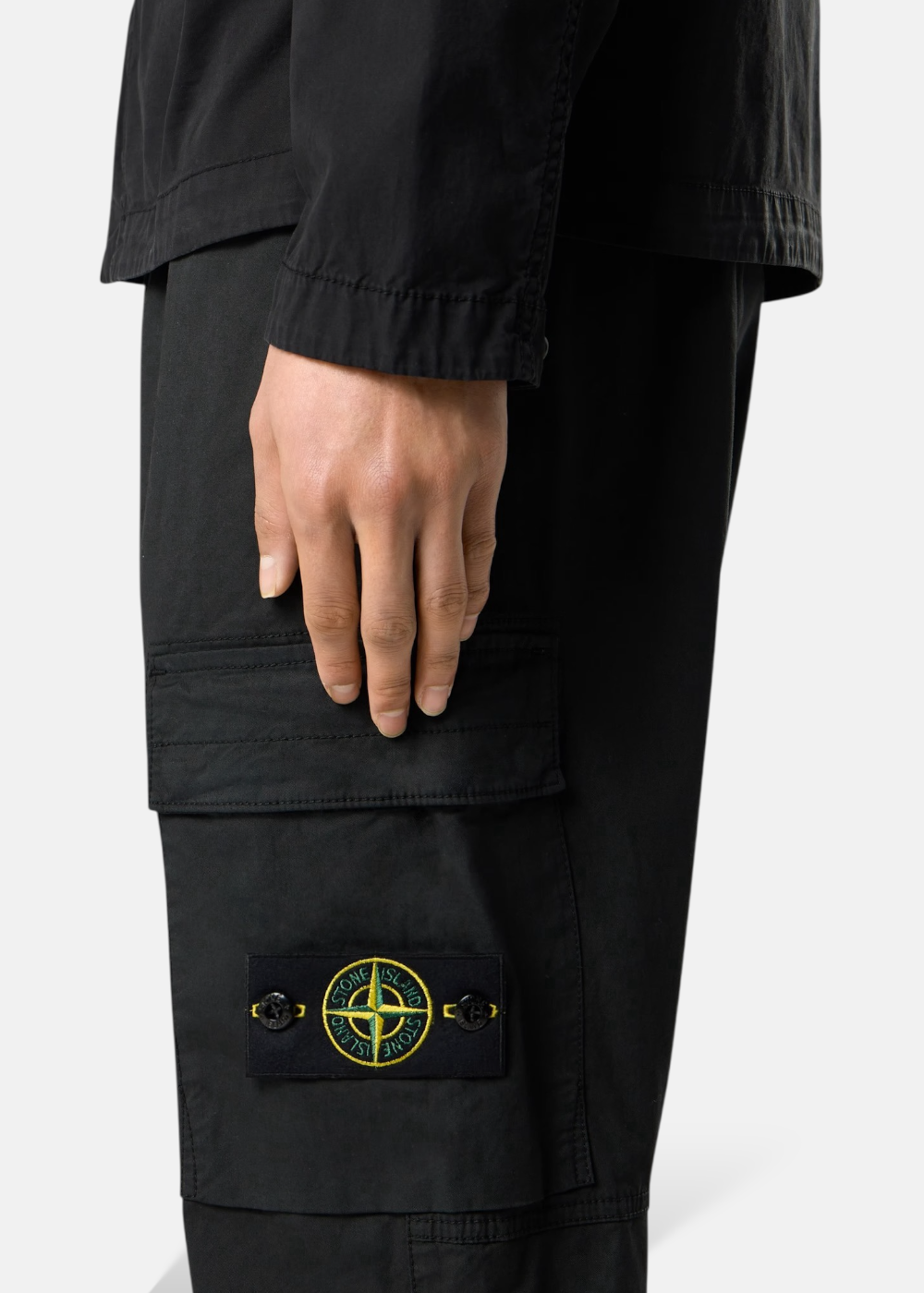 Zoom de profil sur la poche latérale d'un pantalon cargo noir Stone Island porté, mettant en valeur le badge boussole boutonné.