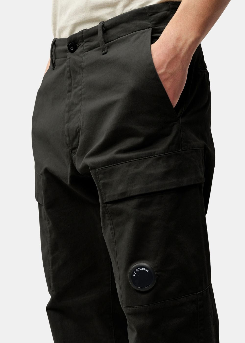 Gros plan sur la poche cargo latérale du pantalon noir C.P. Company affichant la lentille noire signature