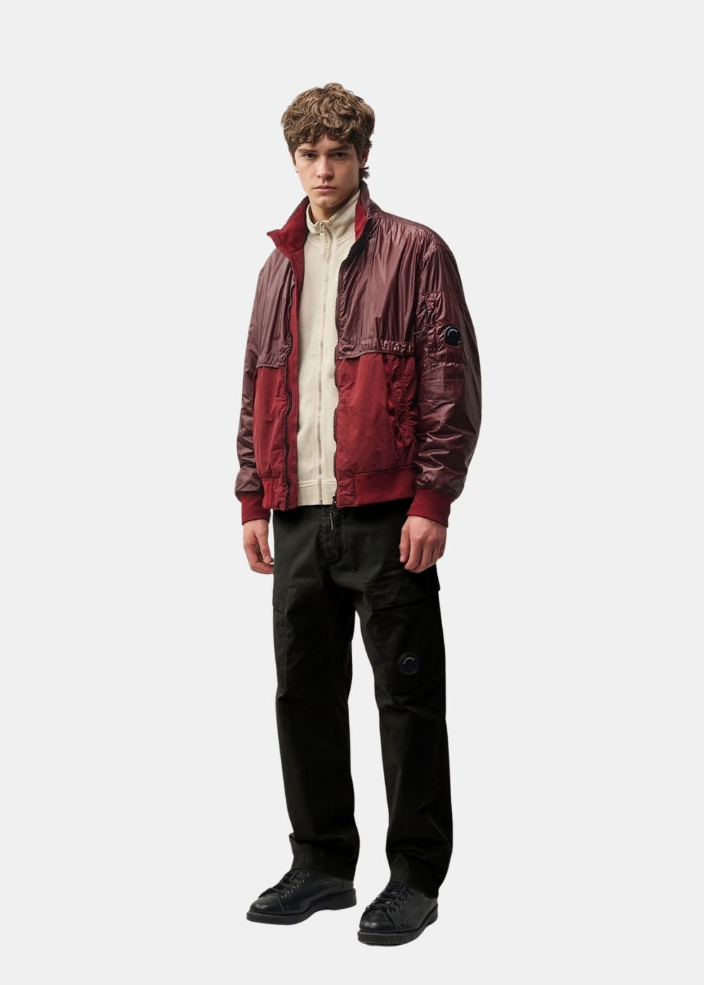 Silhouette complète portée du pantalon cargo C.P. Company noir associant une veste bordeaux et des chaussures noires