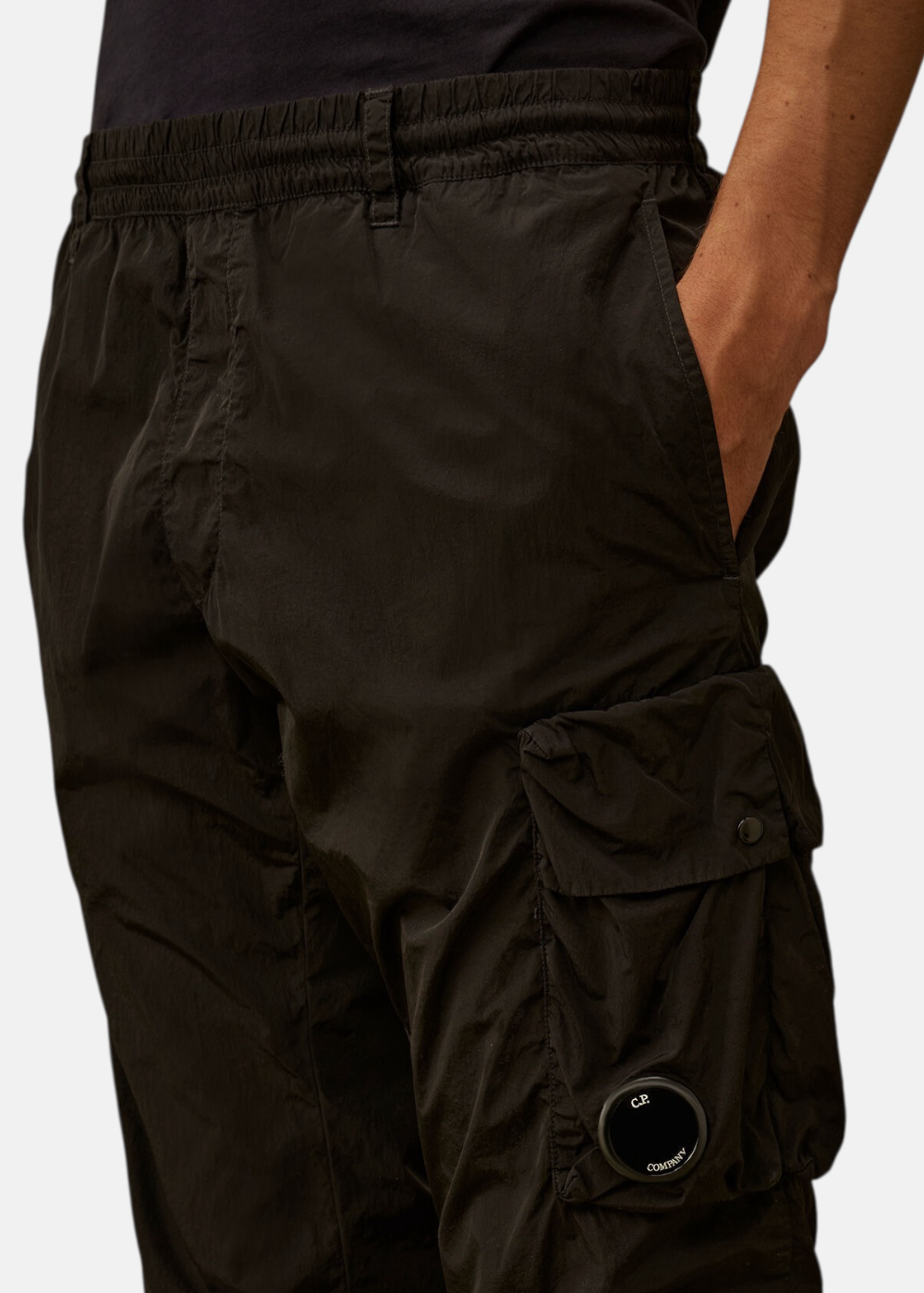 Gros plan sur la poche cargo latérale du pantalon noir avec le détail emblématique Lens de C.P. Company.