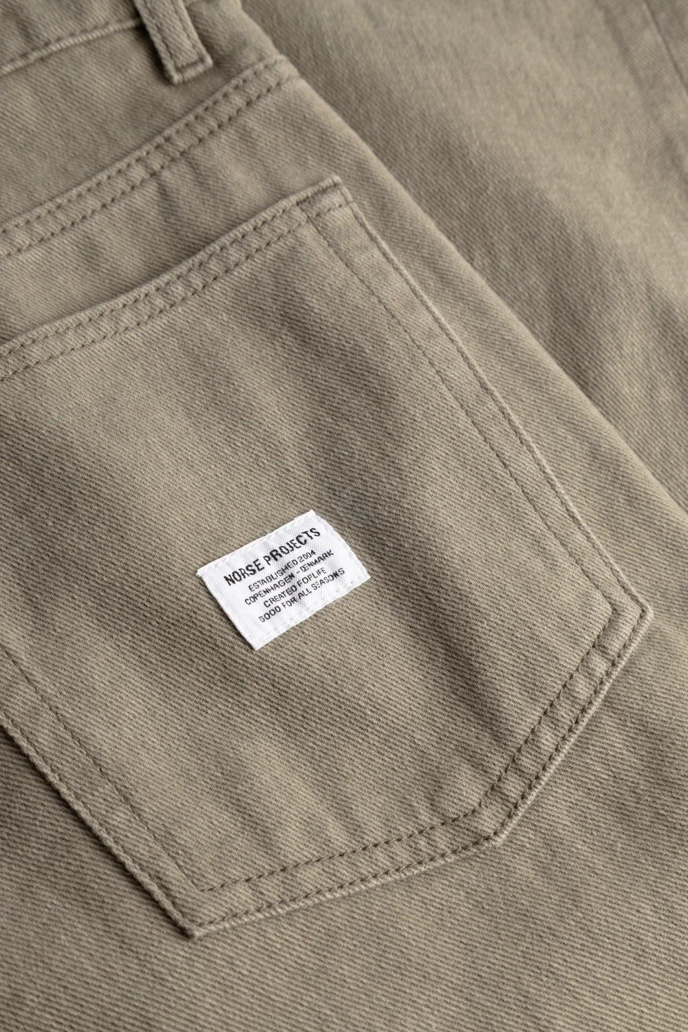 Gros plan sur la poche arrière du pantalon Homme Norse Projects kaki avec étiquette logo blanche tissée.