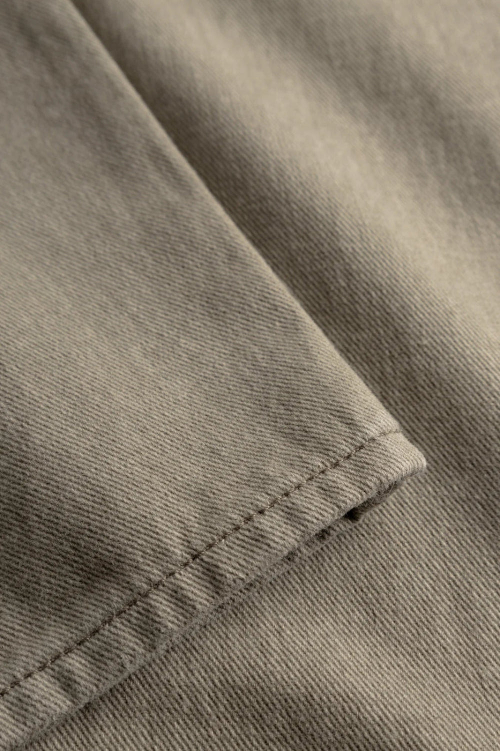Détail rapproché de la texture du twill kaki et des finitions de couture sur l'ourlet du pantalon Homme.