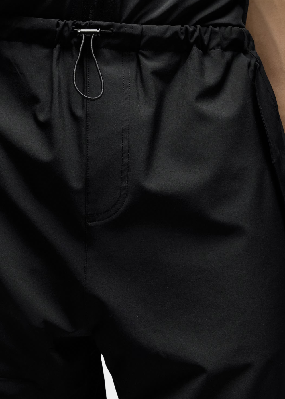 Gros plan sur la ceinture élastique avec cordon de serrage et stoppeur du pantalon outdoor noir.