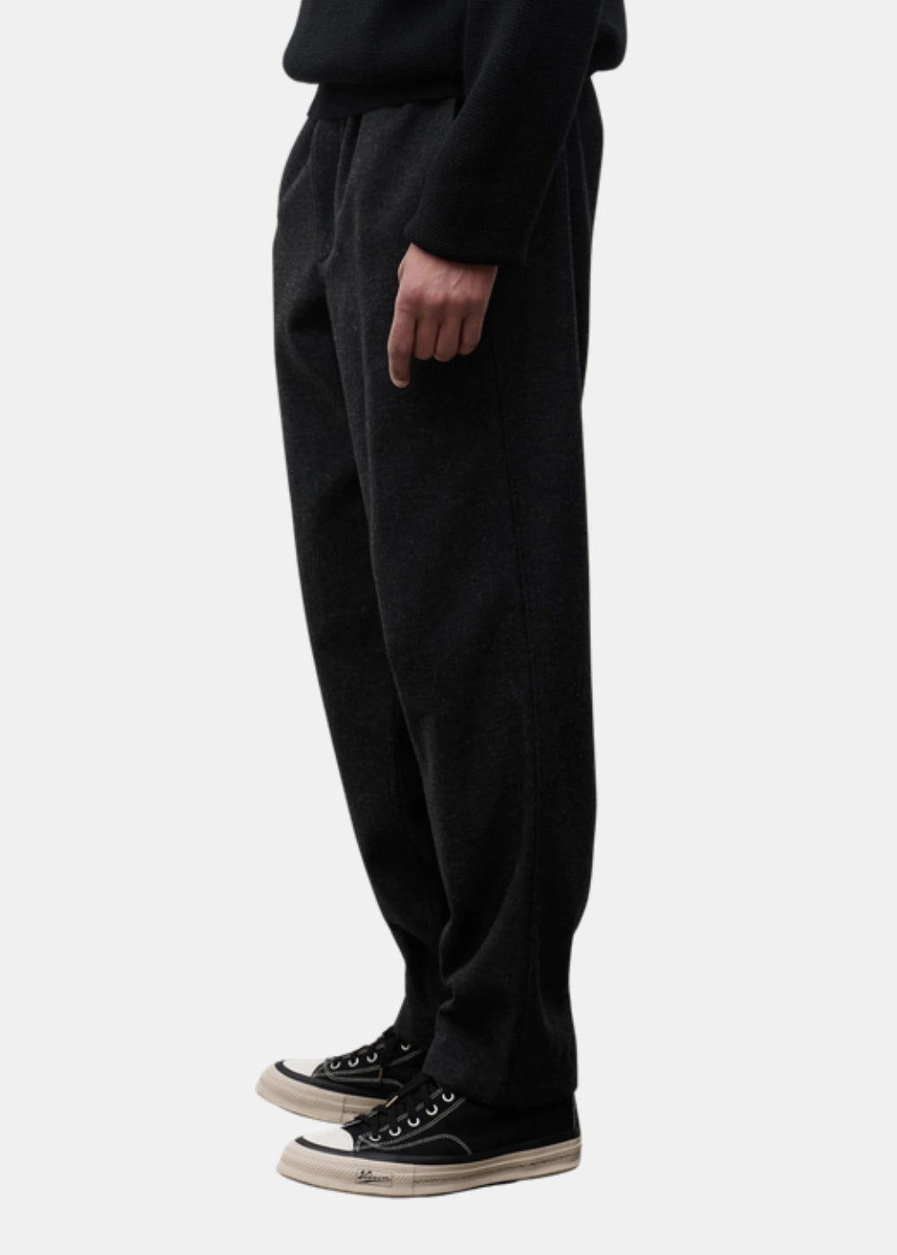 Porté de profil d'un pantalon gris anthracite Norse Projects Trysil, avec baskets noires, montrant la jambe ample et la chute du tissu.