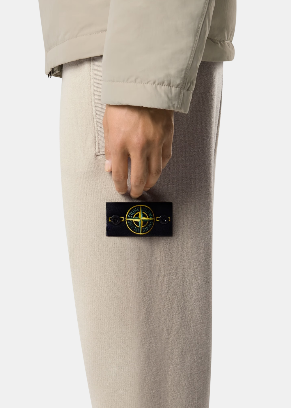 Gros plan sur le badge boussole Stone Island boutonné sur la jambe gauche du pantalon en maille sable