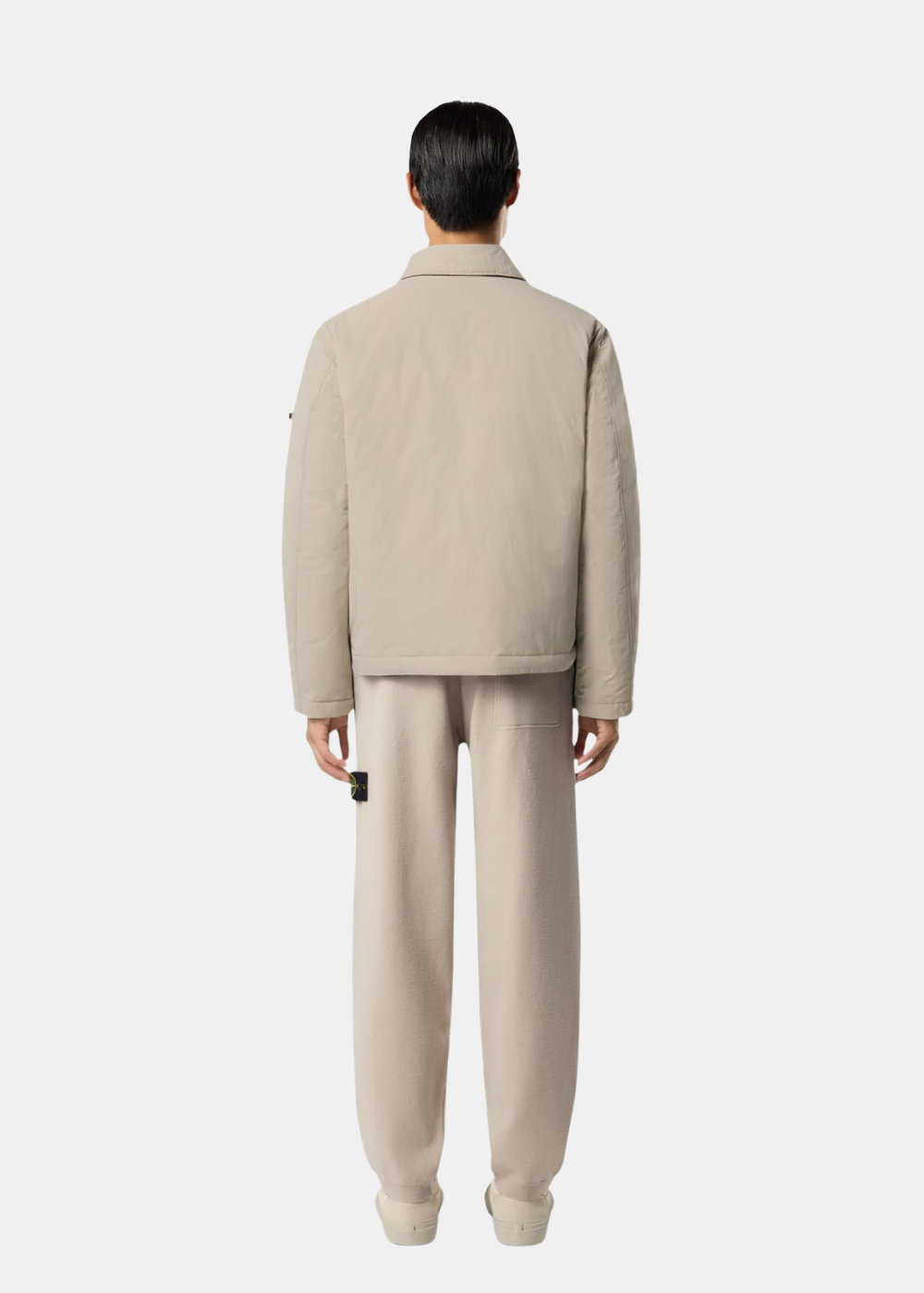 Vue de dos portée du pantalon en maille Stone Island Stretch RWS sable assorti à une veste beige et des baskets claires