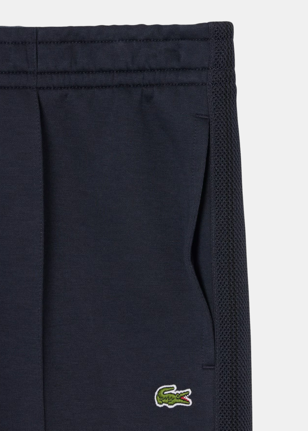 Gros plan sur le logo crocodile classique et la bande latérale texturée du pantalon Lacoste.