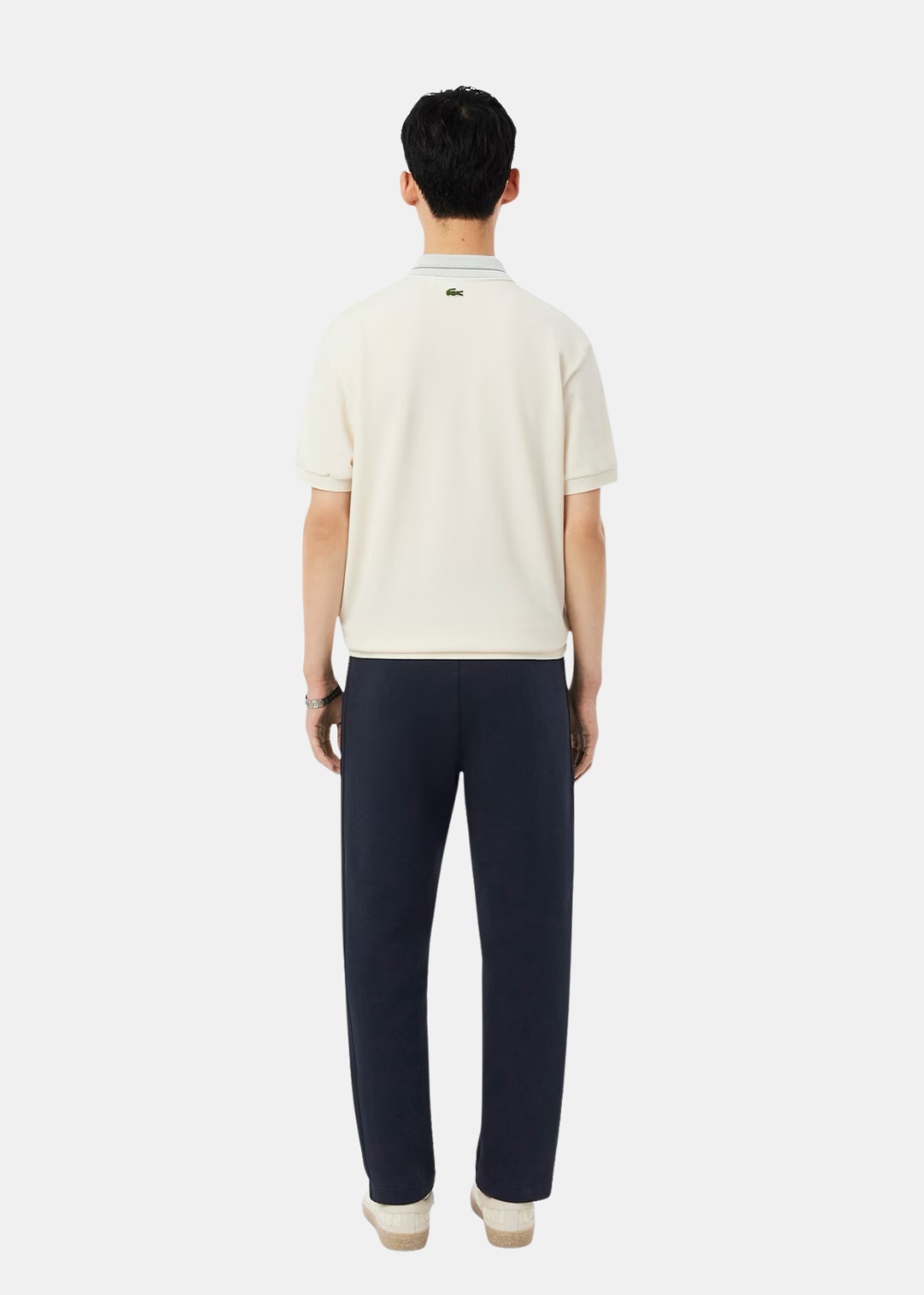 Homme de dos portant le pantalon de survêtement marine Lacoste avec polo crème, coupe droite.