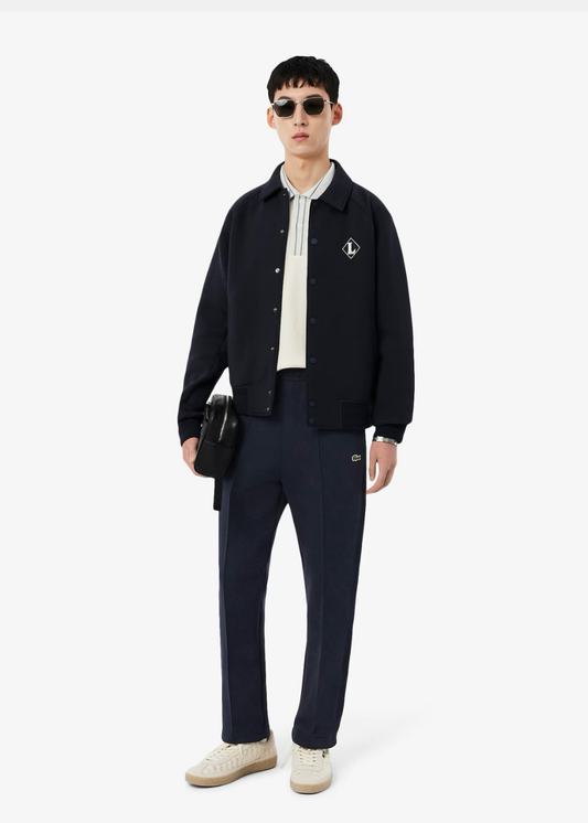 Look complet avec pantalon de survêtement marine Lacoste, blouson assorti et baskets claires.